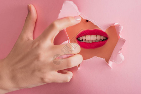 粉红色被隔绝的纸破洞中嘴唇和白牙深背景图片
