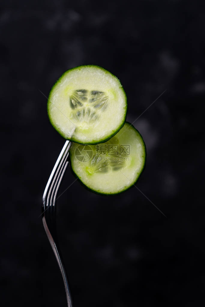 厨房叉子上绿色黄瓜的杯子背着黑暗背图片