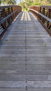 有木甲板和生锈的金属栏杆的垂直框架桥梁在有草的岸湖图片