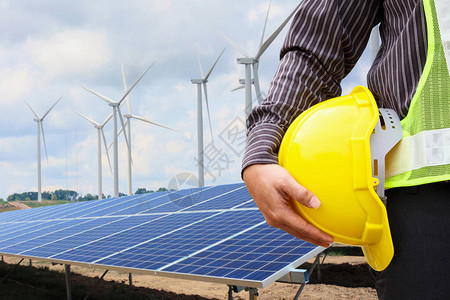 青年商工程师在太阳能电池板和风力发电机发电厂建筑工地背景上持有黄图片