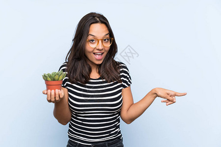 怀着植物的年轻黑头发女人惊讶地拿着一棵植物图片