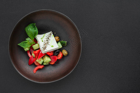 新鲜蔬菜番茄黄瓜罗勒橄榄胡椒黑色碗中的菲塔奶酪希腊沙拉背景图片