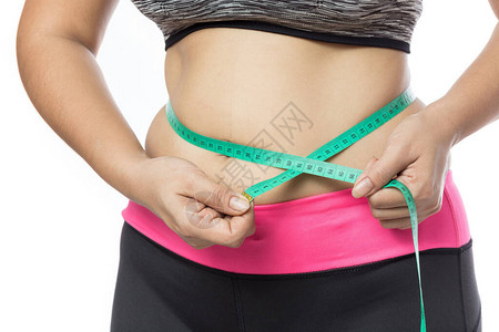 超重女人用绿色测量胶带检查他的身体脂肪在灰色背景的肥胖症图片