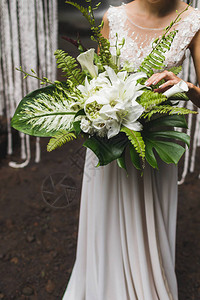 新娘手捧着热带树叶和花朵的花束图片
