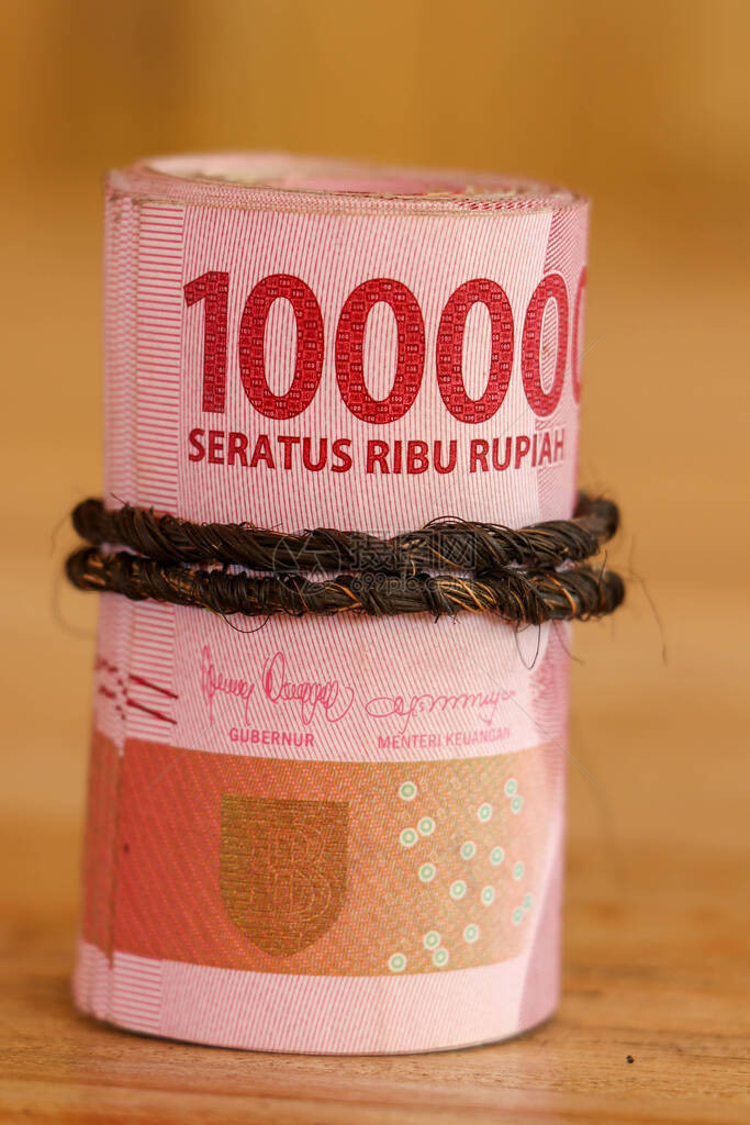 印尼钞票卷成一个管子面值为100000的IDR钞票在旧木背景上用棕色绳子卷起滚动的一叠美元钞票特写镜头图片