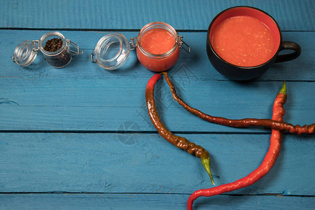 玻璃罐和杯子中木蓝色背景上的红辣椒酱图片