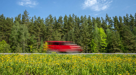 红色小面包车沿着森林沿线的公路行驶图片