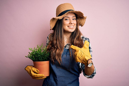穿着围裙和帽子的年轻美丽的褐发农妇拿着盆栽植物图片