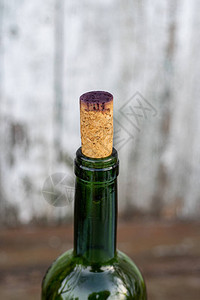 葡萄酒瓶颈的侧视图用深红葡萄酒染色的软木盖封闭透明绿色玻璃瓶特写在苦恼的木图片
