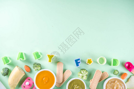 婴幼儿食品有蔬菜水果泥绿色橙色黄色的碗西兰花胡萝卜香蕉苹果用品和玩具绿色背景平躺顶背景图片