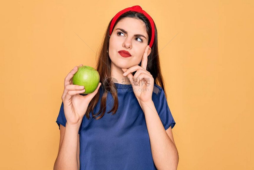 黄色背景下吃新鲜有机健康青苹果的年轻美女严肃地思考问题图片