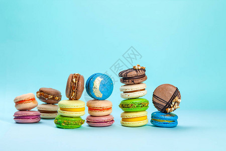 不同类型的五颜六色的甜法式阿克马卡龙或马卡龙在蓝色背景的堆栈中图片
