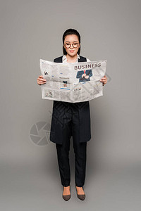在眼镜上看灰色背景报纸的年轻女商人阅读图片