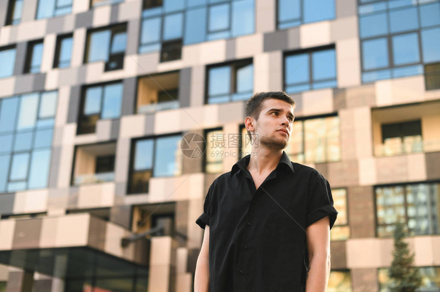 身穿黑色衬衫的男模特站在一栋现代建筑的背景下图片