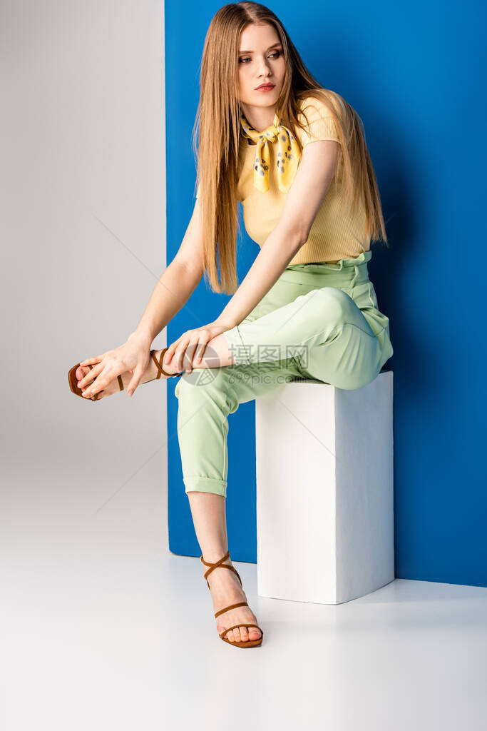 穿着绿色夏季长裤的时尚女和坐在灰色和蓝色白立方体图片