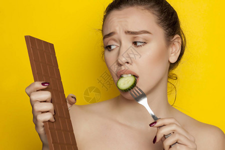 年轻美女吃黄瓜看黄底的朱古力巧克力背景图片