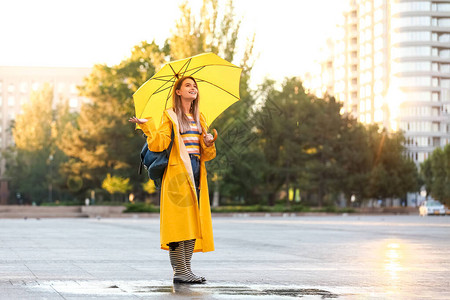 美丽的年轻女子在户外穿着雨衣打着雨伞图片