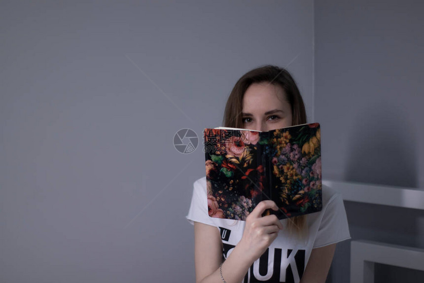 快乐的年轻瘦小女孩用一本书蒙住她的脸图片