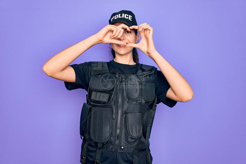 紫色背景上身穿安全防弹背心制服的年轻女警用手和指微笑着透图片