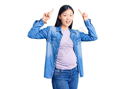 年轻漂亮的女人怀孕期待婴儿微笑惊讶和惊讶并用手指和举图片