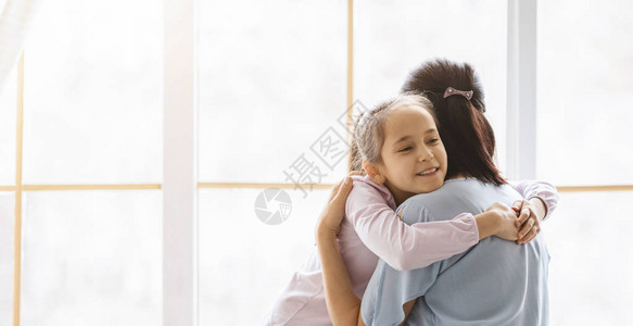 可爱的女儿在家里的窗边用爱和温柔拥抱母亲图片