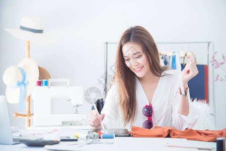 肖像美丽的亚洲设计师女人在裁缝面料时尚小企业店使用平板电脑工作中小图片