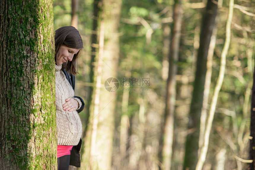 站在一棵树后面的年轻孕妇带着微笑
