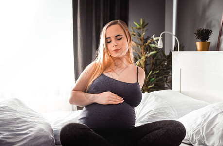 坐在床上抚摸肚子的年轻孕妇图片