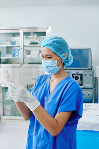 严肃的年轻外科助理在擦洗和医用口罩戴上无菌手图片