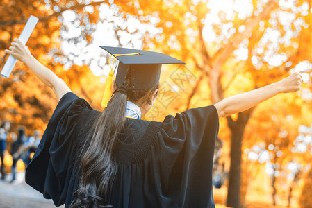 身戴毕业帽子和礼服的毕业生女学生举起手来图片