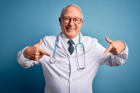 高级灰色头发医生男子身穿听诊器和蓝色背景的医服图片