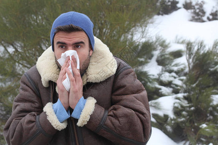 穿着温暖衣服的英俊青年男子在冬天打喷嚏在大自然图片