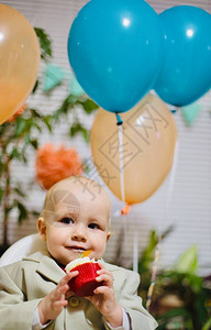 快乐的男婴在喂食椅上吃生日蛋糕和奶油作为他的第一个生日图片