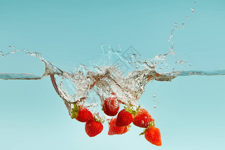 成熟的草莓落入水中蓝色背景上溅起水花图片