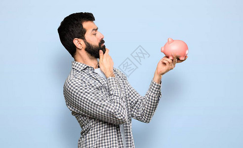 长胡子的帅哥拿着一个小猪银行在孤立图片