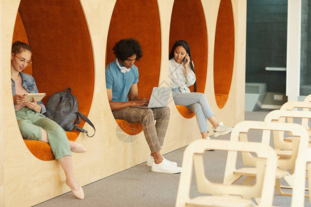 现代多民族学生坐在大学礼堂墙椅内并图片
