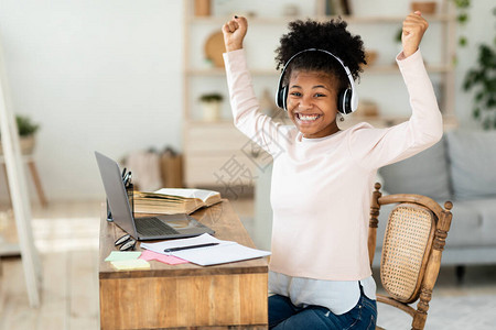 在笔记本电脑上欢乐的黑人女孩握着拳击手在网上课堂学习期间成绩优异在家背景图片
