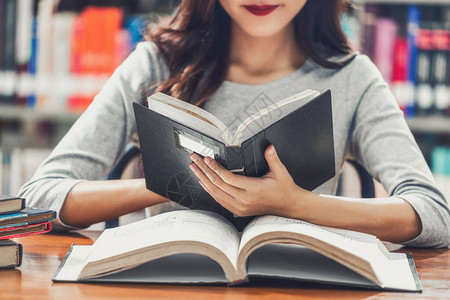 穿着休闲服的亚洲年轻学生在大学图书馆或学院图书馆的木桌上看书图片