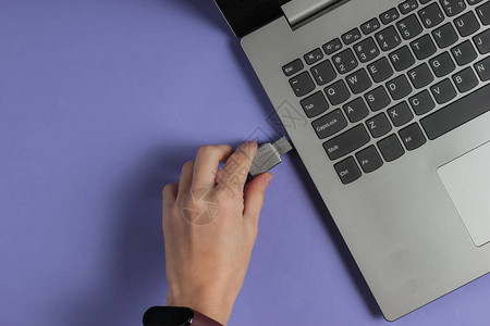 女手将USB闪存驱动器与紫纸背景的笔记本图片