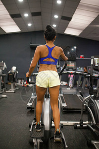 美丽的黑发女人在健身房的椭圆机图片
