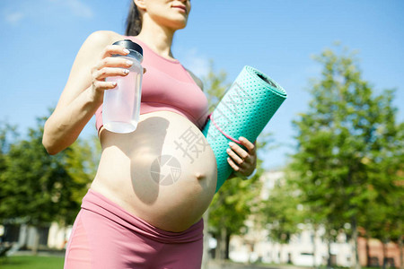 将年轻孕妇关在粉红色顶水瓶和运动垫上图片