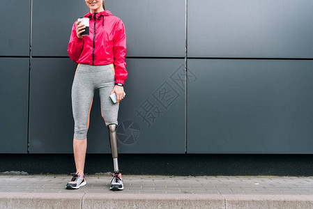 在街上举着杯子和智能手机的残疾运动妇图片