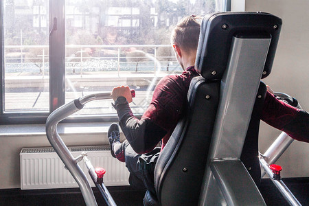 男子坐在长凳上抽肌肉的训练器械健身房照片胸部锻炼与重量他在健身中心图片