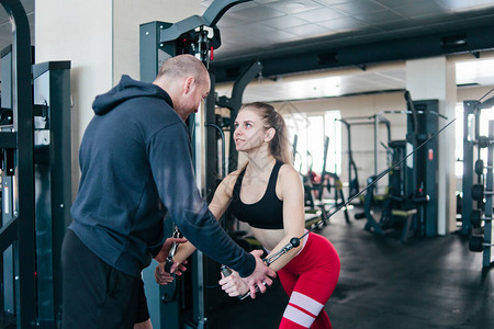 男教练训金发女子在健身房的交叉机中图片