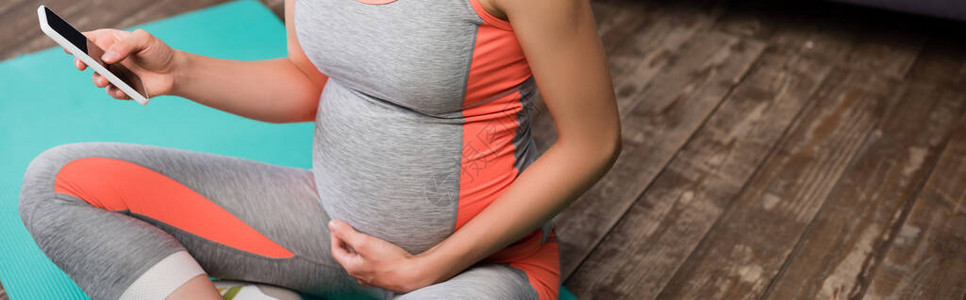 孕妇在坐健身席上时使用智能手机的作物图片