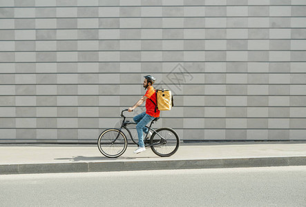 骑自行车的送货员留着胡须和大背包的年轻人在灰色砖墙背景侧视图自由空间的城背景图片