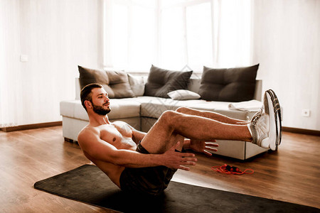 年轻人在家参加体育运动t恤赤膊男运动员在瑜伽垫上锻炼腹肌的照片锻炼身体的大一新生在阳光明媚的公图片