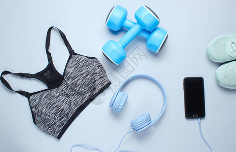 健身理念带有耳机塑料哑铃运动胸罩灰色背景运动鞋的智能手机图片