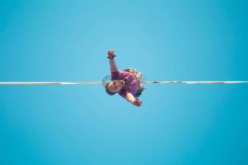 Highliner从下面的蓝天视图垂悬一个人在伸展的吊索上前进走钢丝者的坠落一个人在悬崖边上保图片
