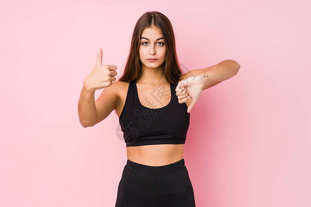 做运动的年轻caucasian健身女单独显示拇指向上和拇指向下图片